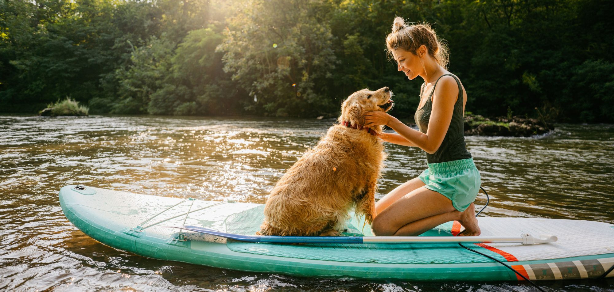 A woman and her dog kneeling on a paddle board.